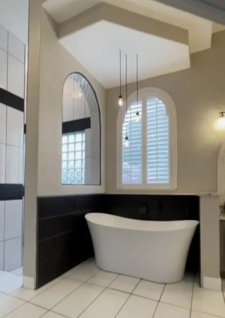 Freestanding tub framed by black tile and arched windows