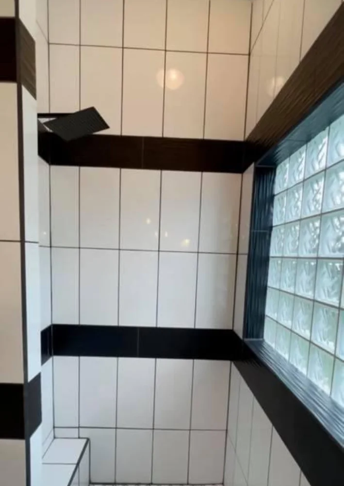 White shower tile with dark accent band beside glass-block window