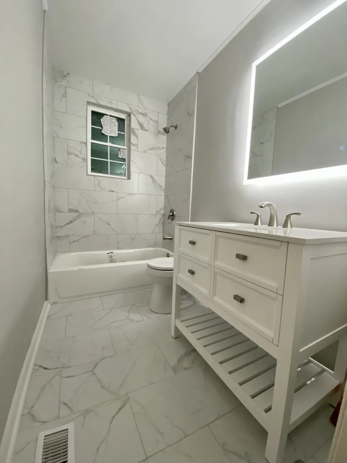 Bright renovated bathroom with marble-look tile and illuminated mirror